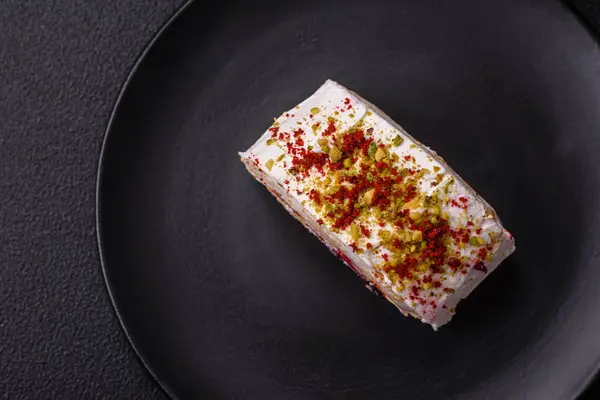 A piece of delicious sweet meringue roll with mascarpone cheese, berries and almonds on a dark concrete background