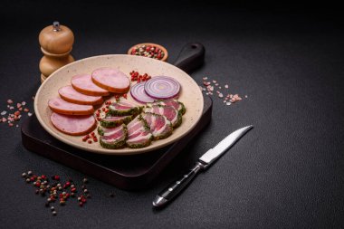 Tuzlu ve baharatlı lezzetli füme sosis koyu beton arka planda dilimler halinde kesilmiş.