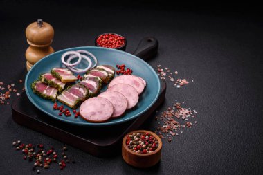 Tuzlu ve baharatlı lezzetli füme sosis koyu beton arka planda dilimler halinde kesilmiş.