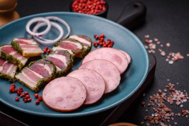 Tuzlu ve baharatlı lezzetli füme sosis koyu beton arka planda dilimler halinde kesilmiş.