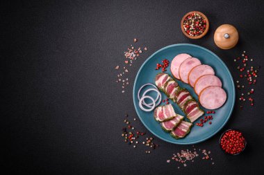 Tuzlu ve baharatlı lezzetli füme sosis koyu beton arka planda dilimler halinde kesilmiş.