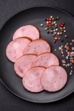 Tuzlu ve baharatlı lezzetli füme sosis koyu beton arka planda dilimler halinde kesilmiş.