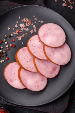 Tuzlu ve baharatlı lezzetli füme sosis koyu beton arka planda dilimler halinde kesilmiş.