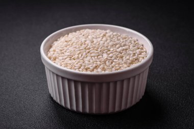 Yuvarlak bir seramik kasede, koyu beton arka planda pişmemiş beyaz pirinç. Asya yemeği pişirmek