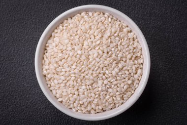 Yuvarlak bir seramik kasede, koyu beton arka planda pişmemiş beyaz pirinç. Asya yemeği pişirmek