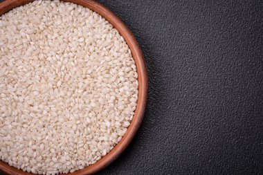 Yuvarlak bir seramik kasede, koyu beton arka planda pişmemiş beyaz pirinç. Asya yemeği pişirmek