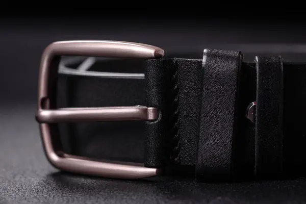 New leather men\'s belt with an old-style metal buckle on a dark concrete background