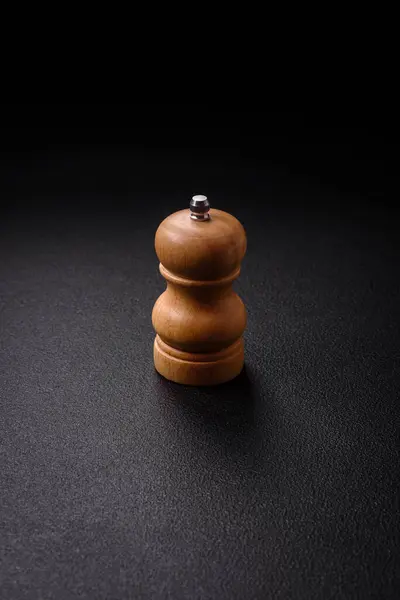Beautiful wooden figured pepper shaker or salt shaker with a mill on a dark textured background