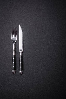 Çelikten yapılmış mutfak bıçağı ve çatalı. Arka planı koyu beton.