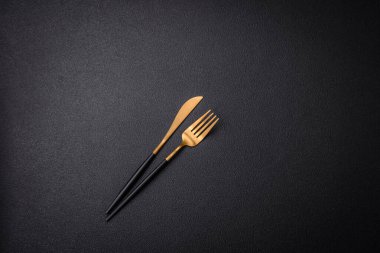 Çelikten yapılmış mutfak bıçağı ve çatalı. Arka planı koyu beton.