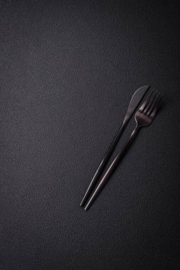 Çelikten yapılmış mutfak bıçağı ve çatalı. Arka planı koyu beton.