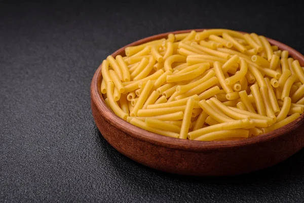 Raw whole grain wheat pasta with salt and spices in a ceramic plate on a dark textured background