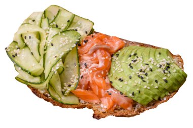 Delicious brown bread toast with salmon, avocado, cucumber and sesame seeds on a textured concrete background