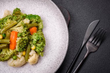 Delicious fresh vegetables steamed carrots, broccoli, cauliflower on a black plate on a dark concrete background