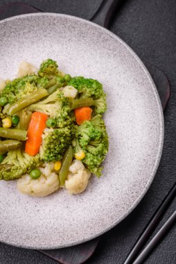 Delicious fresh vegetables steamed carrots, broccoli, cauliflower on a black plate on a dark concrete background
