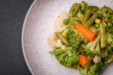 Delicious fresh vegetables steamed carrots, broccoli, cauliflower on a black plate on a dark concrete background