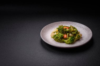 Delicious fresh vegetables steamed carrots, broccoli, cauliflower on a black plate on a dark concrete background