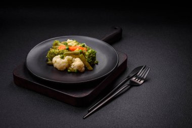 Delicious fresh vegetables steamed carrots, broccoli, cauliflower on a black plate on a dark concrete background