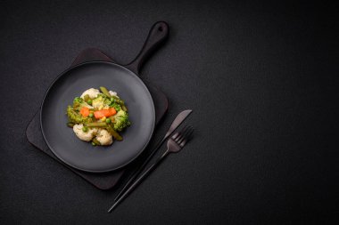 Delicious fresh vegetables steamed carrots, broccoli, cauliflower on a black plate on a dark concrete background