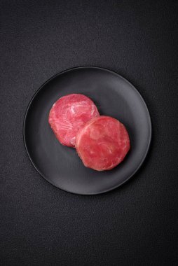 Koyu beton arka planda tuzlu ve baharatlı çiğ ton balıklı yuvarlak biftekler.