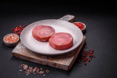 Koyu beton arka planda tuzlu ve baharatlı çiğ ton balıklı yuvarlak biftekler.