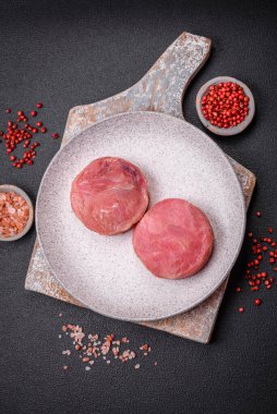 Koyu beton arka planda tuzlu ve baharatlı çiğ ton balıklı yuvarlak biftekler.