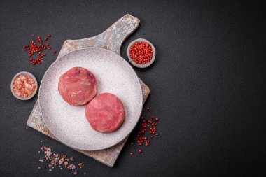 Koyu beton arka planda tuzlu ve baharatlı çiğ ton balıklı yuvarlak biftekler.