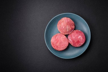 Koyu beton arka planda tuzlu ve baharatlı çiğ ton balıklı yuvarlak biftekler.