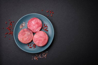 Koyu beton arka planda tuzlu ve baharatlı çiğ ton balıklı yuvarlak biftekler.