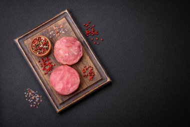 Koyu beton arka planda tuzlu ve baharatlı çiğ ton balıklı yuvarlak biftekler.