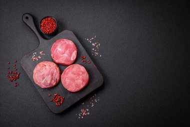 Koyu beton arka planda tuzlu ve baharatlı çiğ ton balıklı yuvarlak biftekler.