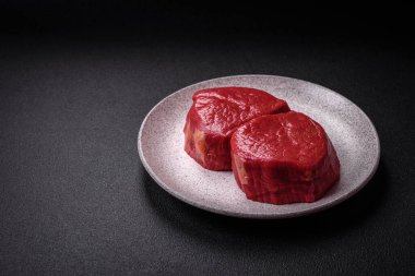 Taze taze çiğ fileminyon, arka planda tuz, baharat ve otlarla birlikte.