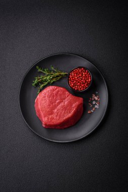 Taze taze çiğ fileminyon, arka planda tuz, baharat ve otlarla birlikte.