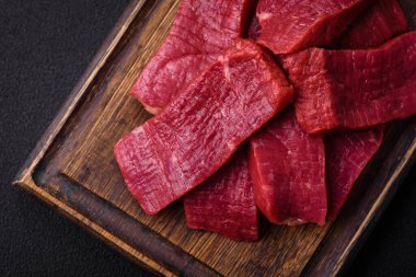 Tuz, baharat ve otlarla sulu taze çiğ et, koyu dokulu beton arka planda.