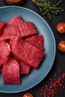 Tuz, baharat ve otlarla sulu taze çiğ et, koyu dokulu beton arka planda.