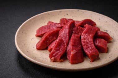 Tuz, baharat ve otlarla sulu taze çiğ et, koyu dokulu beton arka planda.