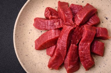 Tuz, baharat ve otlarla sulu taze çiğ et, koyu dokulu beton arka planda.