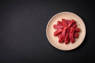 Tuz, baharat ve otlarla sulu taze çiğ et, koyu dokulu beton arka planda.