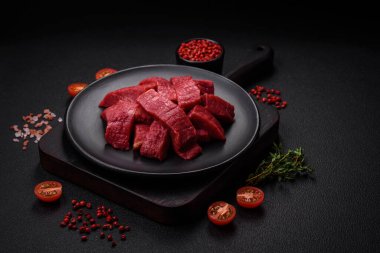 Tuz, baharat ve otlarla sulu taze çiğ et, koyu dokulu beton arka planda.