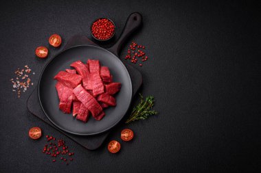 Tuz, baharat ve otlarla sulu taze çiğ et, koyu dokulu beton arka planda.