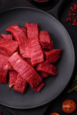 Tuz, baharat ve otlarla sulu taze çiğ et, koyu dokulu beton arka planda.