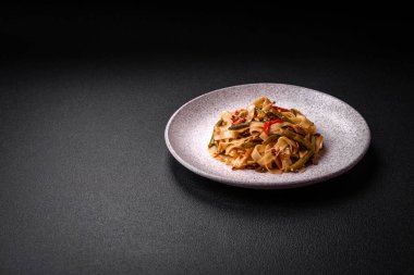 Lezzetli Asya yemeği udonu acı biber, yeşil fasulye, baharat ve otlar seramik tabakta koyu beton arka planda.