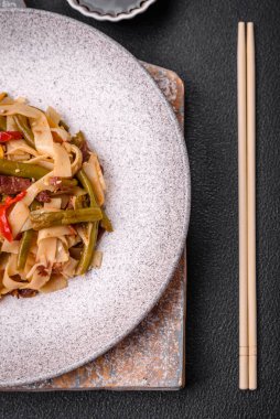 Lezzetli Asya yemeği udonu acı biber, yeşil fasulye, baharat ve otlar seramik tabakta koyu beton arka planda.