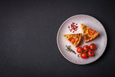 Koyu beton arka planda domates, peynir, tavuk, baharat ve bitkilerle nefis kiş.