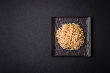 Lezzetli Asya mutfağı. İçinde pirinç, erişte, biber, mantar ve baharatlar var. Koyu beton arka planda.