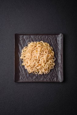 Lezzetli Asya mutfağı. İçinde pirinç, erişte, biber, mantar ve baharatlar var. Koyu beton arka planda.