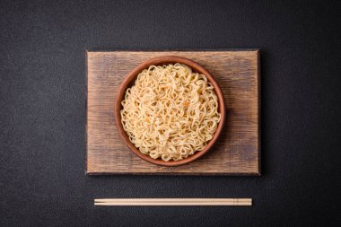 Lezzetli Asya mutfağı. İçinde pirinç, erişte, biber, mantar ve baharatlar var. Koyu beton arka planda.