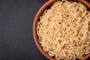 Lezzetli Asya mutfağı. İçinde pirinç, erişte, biber, mantar ve baharatlar var. Koyu beton arka planda.