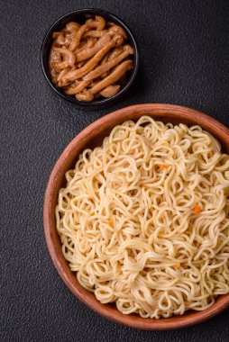 Lezzetli Asya mutfağı. İçinde pirinç, erişte, biber, mantar ve baharatlar var. Koyu beton arka planda.