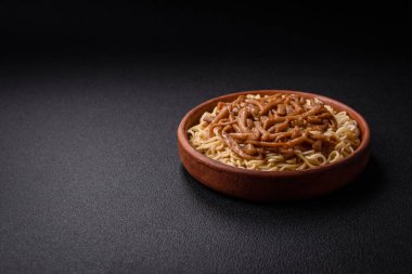 Lezzetli Asya mutfağı. İçinde pirinç, erişte, biber, mantar ve baharatlar var. Koyu beton arka planda.